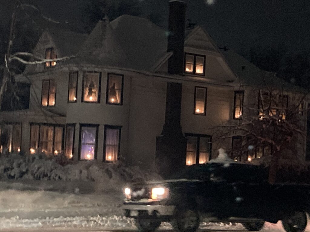 A snowy pickup passes by a Victorian style home near downtown Alexandria MN with candles in every window. 